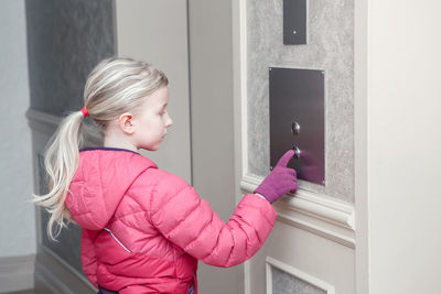 Side view of girl pushing button by elevator