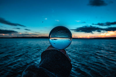 Close-up of person wearing sunglasses against sea during sunset