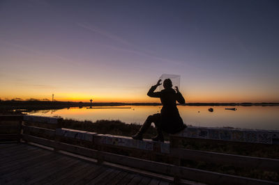 Rear view of silhouette woman standing on railing against sky during sunset