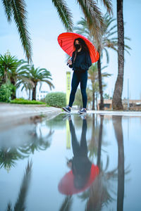 Woman with a mask and a red umbrella reflected on a puddle