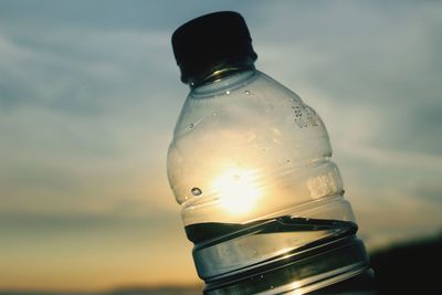 Close-up of water bottle against sky during sunset