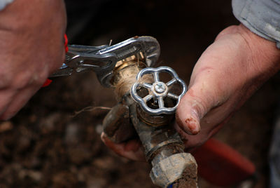 Cropped hands using pliers on pipe at field