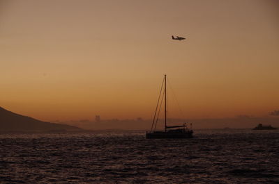 Silhouettes sailboat in sea anove a plain against sky during sunset