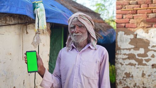 Old asian man smiling and showing a green screen cell phone with rural village life concept backgro