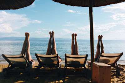 Four girls with legs in the air, sitting in chairs on beach 