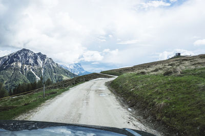 Car on dirt road against cloudy sky