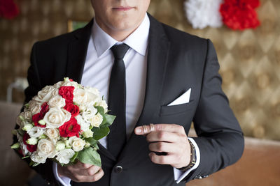 Midsection of bridegroom holding bouquet with wedding rings