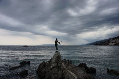 Man standing on rock at beach against cloudy sky