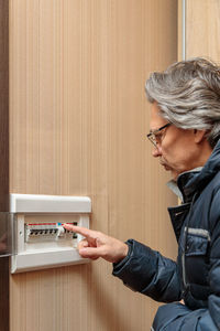 An adult man in a warm jacket looks at the electrical panel. energy saving concept. expensive 