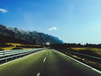 Road leading towards mountains against blue sky