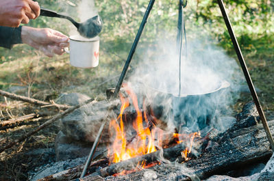 Cropped hands of person making soup on campfire in forest