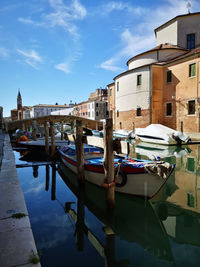 Boats moored in canal by city against sky