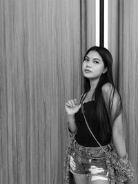 Portrait of young woman standing against wall