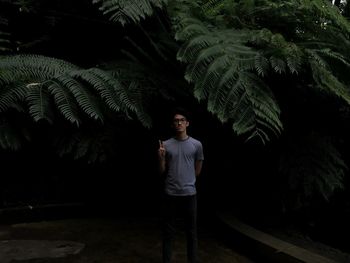 Portrait of young man gesturing peace sign while standing against trees at night