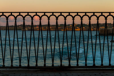 Railing by swimming pool against sky during sunset