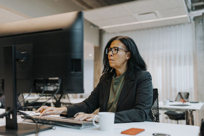 Confident senior businesswoman using computer while sitting at desk in corporate office