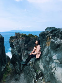 Woman sitting on rock by sea against sky