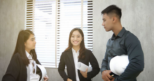 Young smiling architects discussing while standing at office