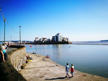 People by sea against clear sky