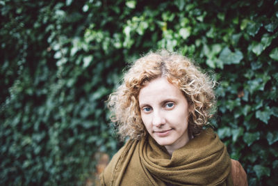 Portrait of smiling woman with curly hair against plants