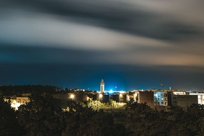 Illuminated buildings by sea against sky at night