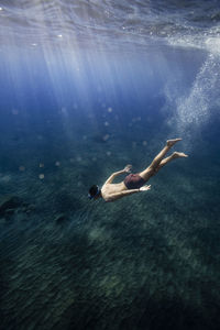 Sunlight on young man swimming over ocean floor in sea