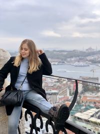 Young woman sitting in city against sky