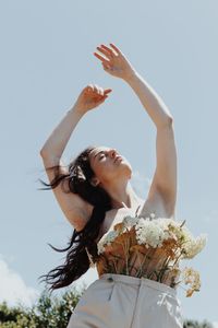 Low angle view of woman with arms raised against sky