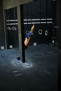 Shirtless fit young man working out hanging with rings upside down