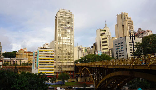 Bridge over river by buildings against sky in city