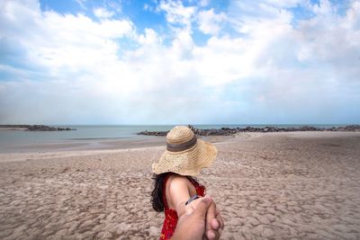 Woman wearing hat holding hands while standing at beach