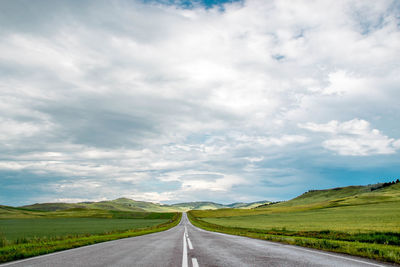 Empty road amidst field against sky