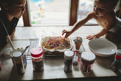 Two siblings sneaking sprinkles off of freshly baked cake treat