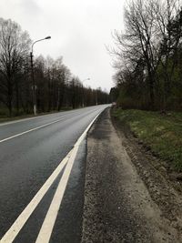 Empty road by trees in city against sky