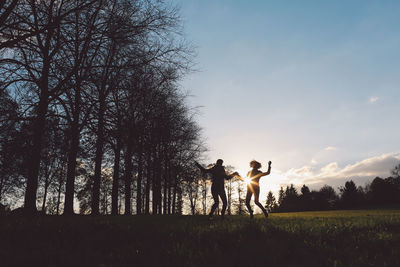 Silhouette women jumping over grass at les jardins d annevoie against sky