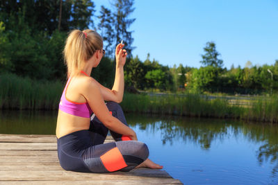 Woman sitting by lake against sky