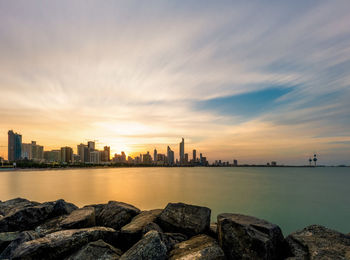 Sea by buildings against sky during sunset