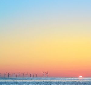 Wind turbines by sea against clear sky during sunset