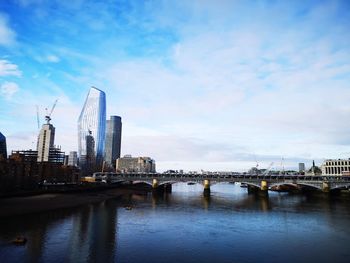 Bridge over river by buildings against sky