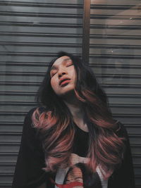 Young woman looking away while standing against wall