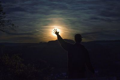 Silhouette man standing in sunlight against sky during sunset