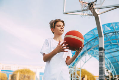 Low angle view of boy playing with basketball against sky