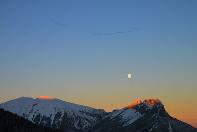 Scenic view of snowcapped mountains against clear sky during sunrise