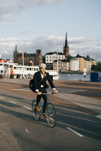 Full length of businessman riding bicycle on street in city against sky