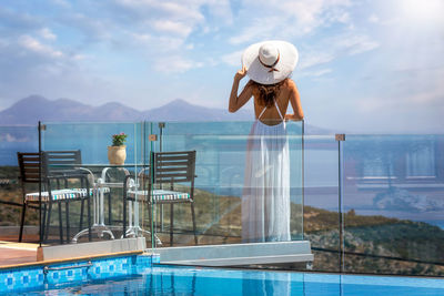 Rear view of woman standing by swimming pool against sky