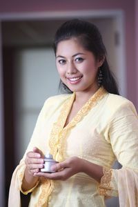 Portrait of young woman holding oil lamp while standing at home