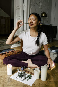 Young woman smelling herbs while sitting on exercise mat at home