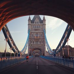 Rear view of cyclist riding bicycle on tower bridge against sky at morning