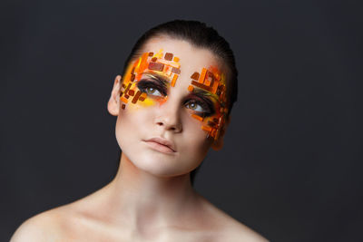 Close-up of shirtless young woman with eye make-up and rhinestones against gray background