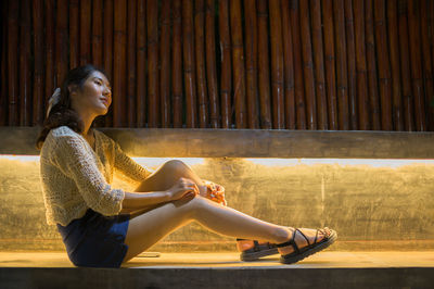 Side view of young woman sitting on wooden floor